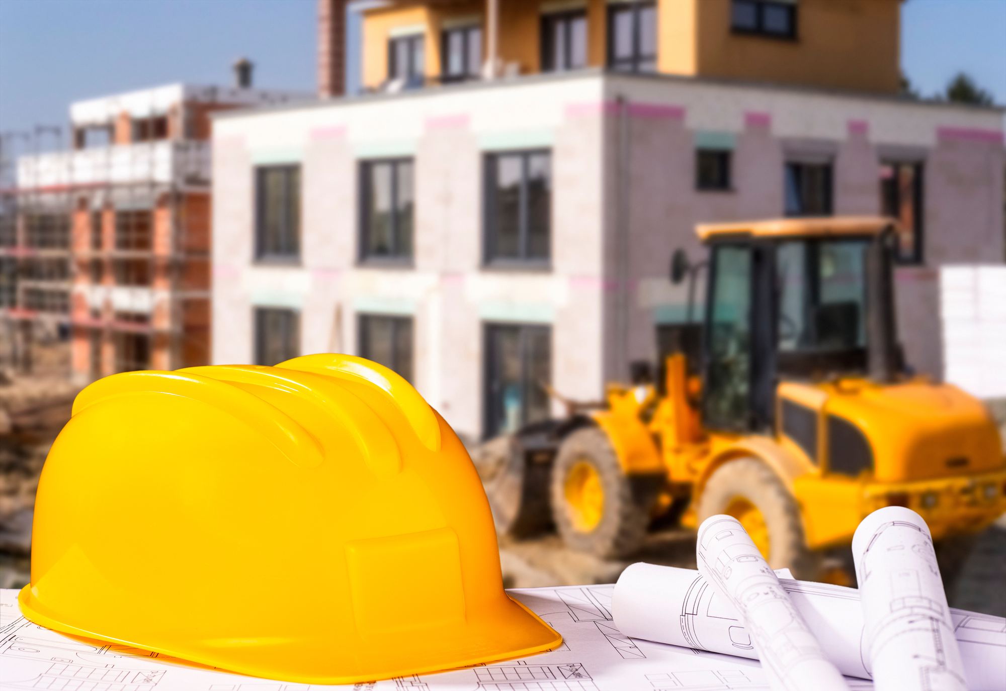 Bauhelm und Baupläne vor einer Baustelle im Rohbau